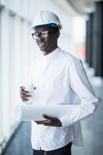 Young Afro-American engineer with blue prints in front of panora